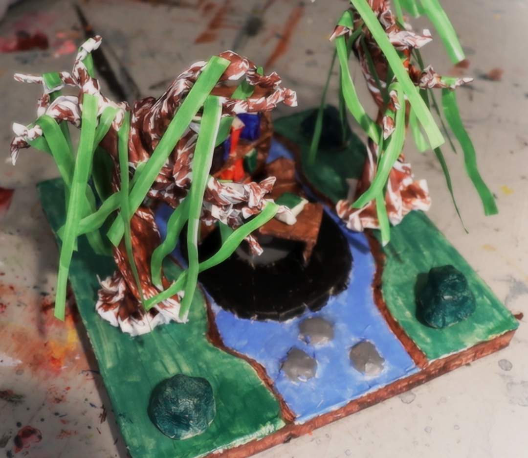 A clay model featuring a blue stream and green grass with green trees.