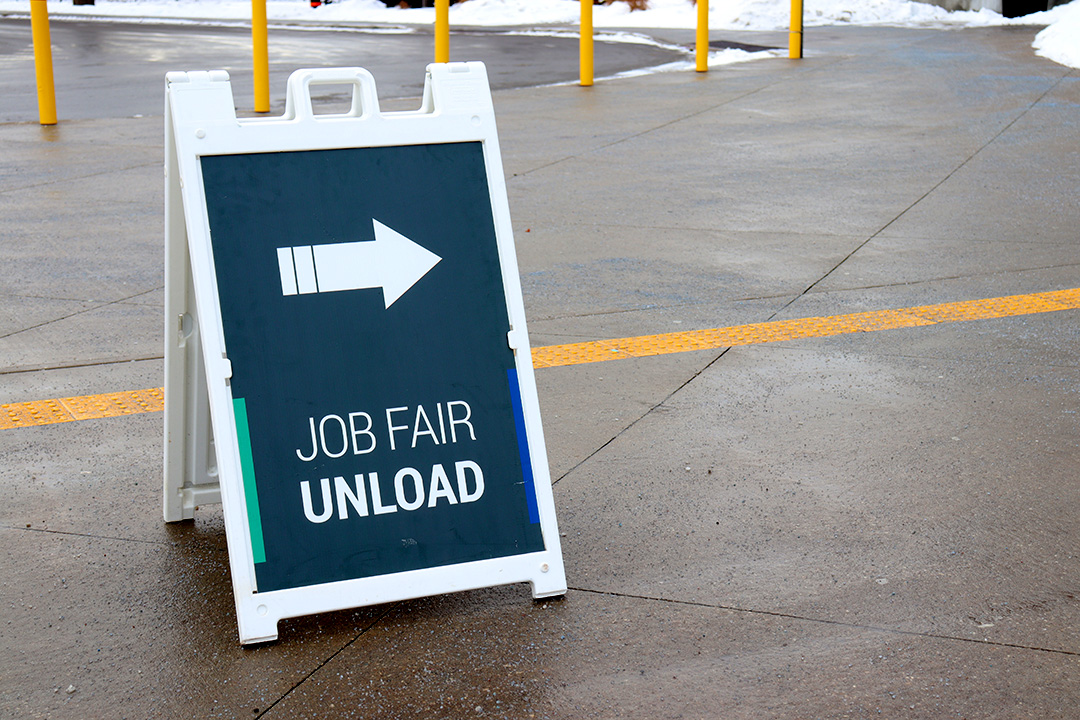 A navy sign with a white border, an arrow and the words "Job Fair Unload" sits on a sidewalk