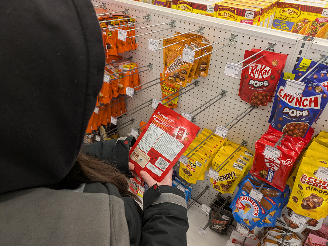 A woman stands in a candy aisle holding a bag of "KitKat Pops" looking at the nutrition label.