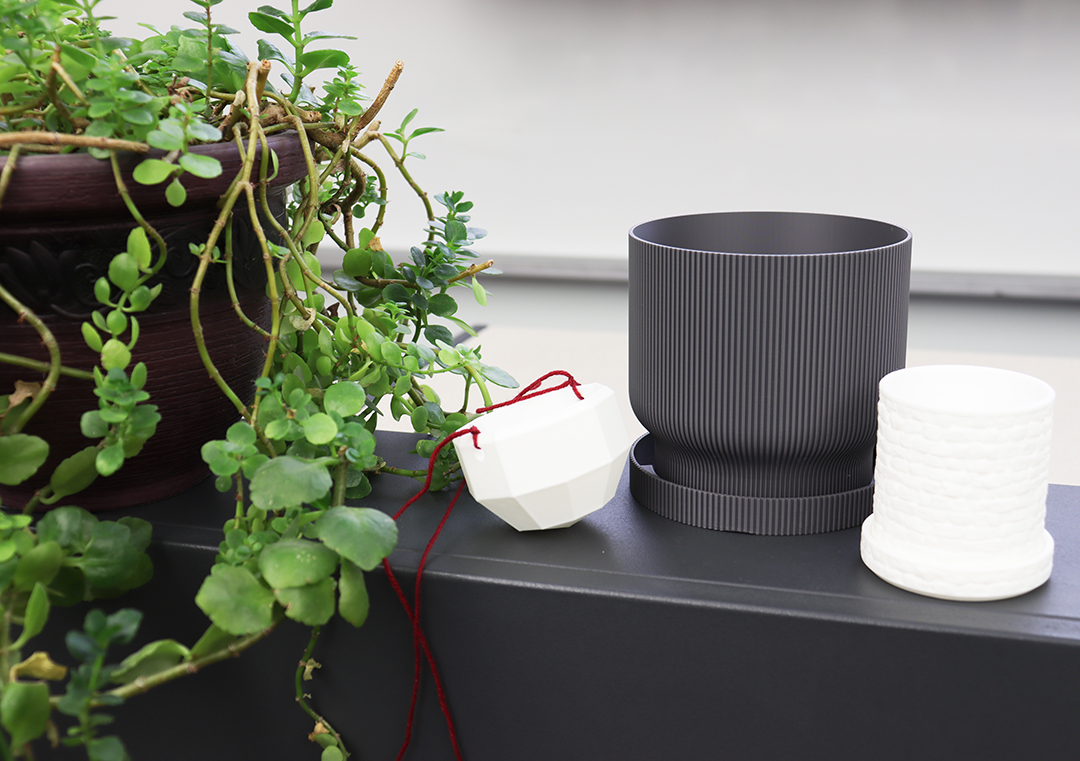 A display of three different 3D printed planters. One on the left is white and has a string so it can hang, the one in the middle is grey and the one of the right is white.