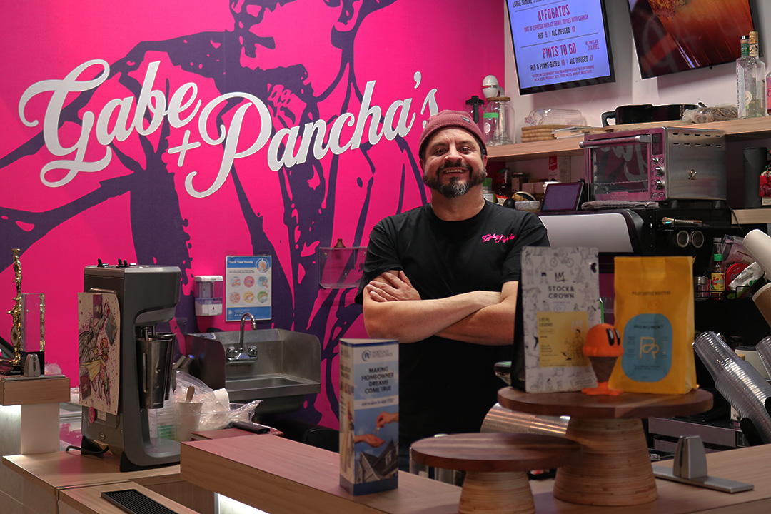 A man in a black shirt faces the camera smiling. His arms are folded across his chest. A sign reading 'Gabe and Pancha's' is in the background.