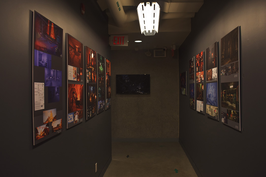 A hallway with colorful game art layouts posted on grey walls.