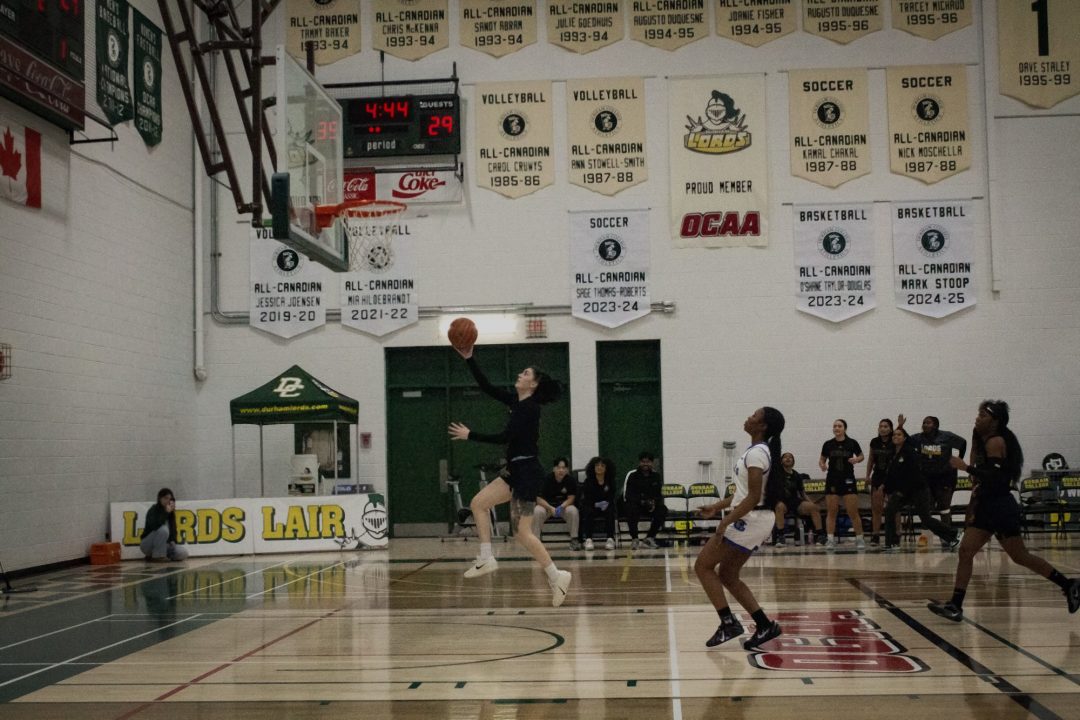 A young woman holding a basketball takes flight to sink a basket.