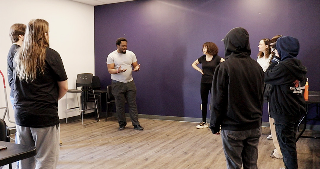 People stand in a circle in a room with a white wall and a purple wall.