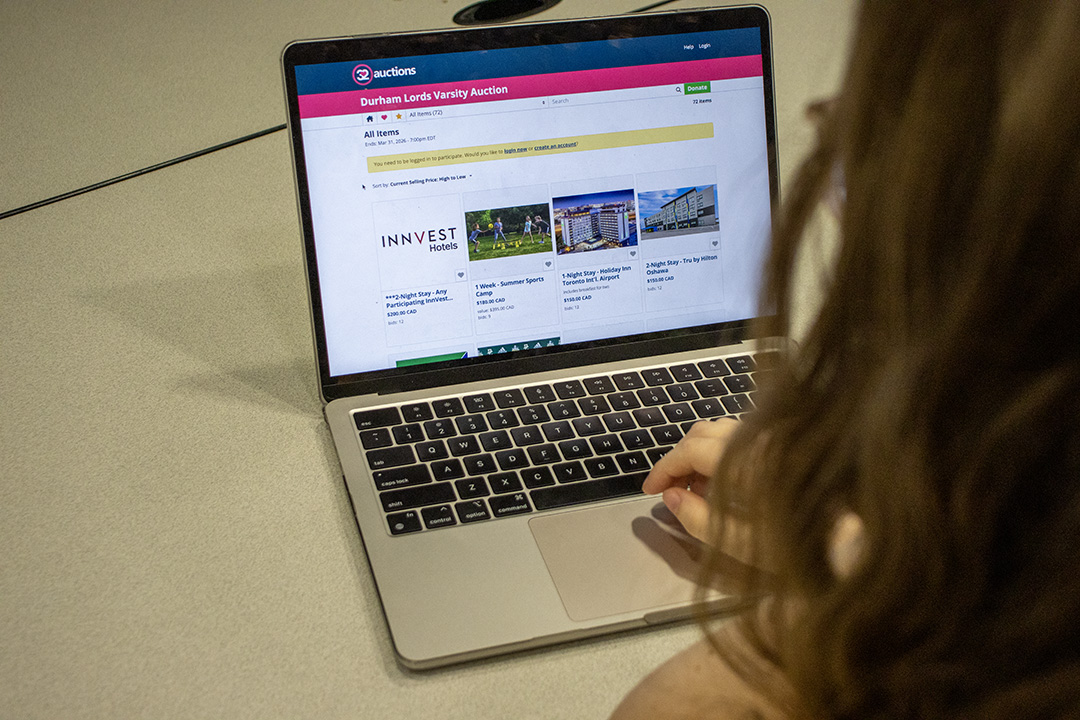 Looking over the shoulder of a student looking at the Varsity Auction website on a laptop.