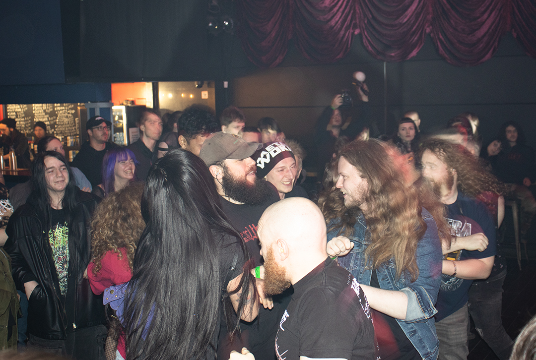 A crowd of people in a dark venue are running in a circle and smiling as they enjoy a performance