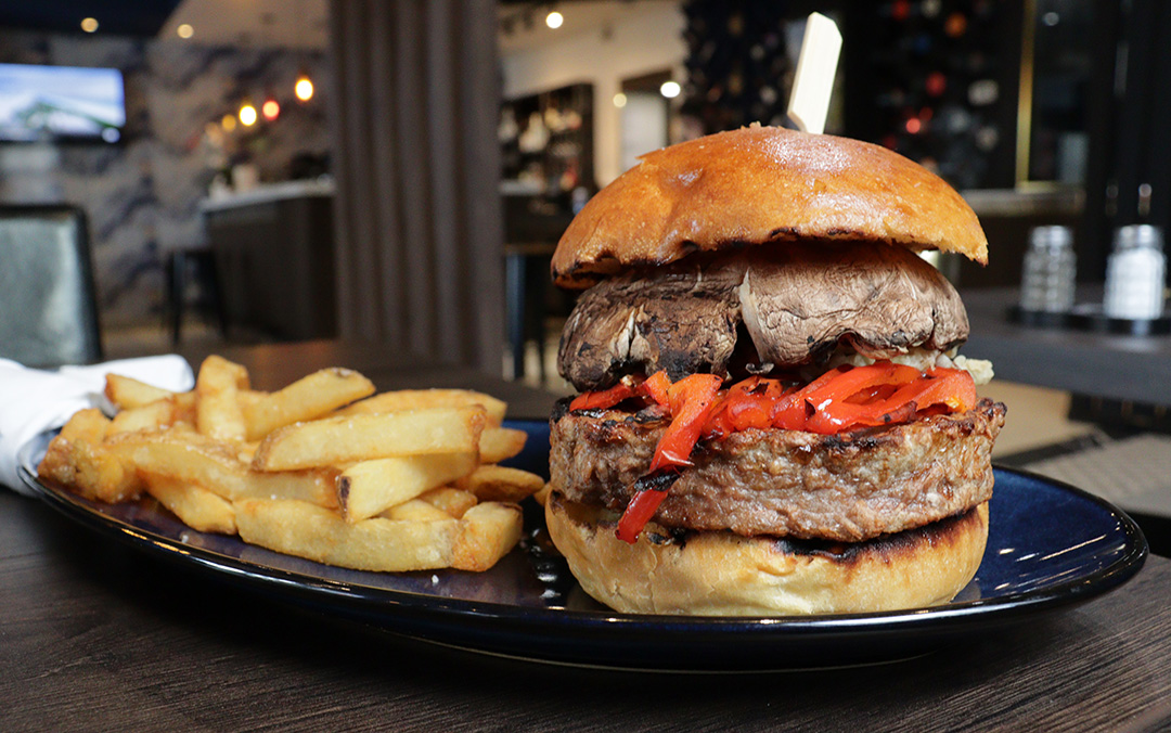 A veggie burger with portobello mushrooms and peppers sits on a plate beside fries.