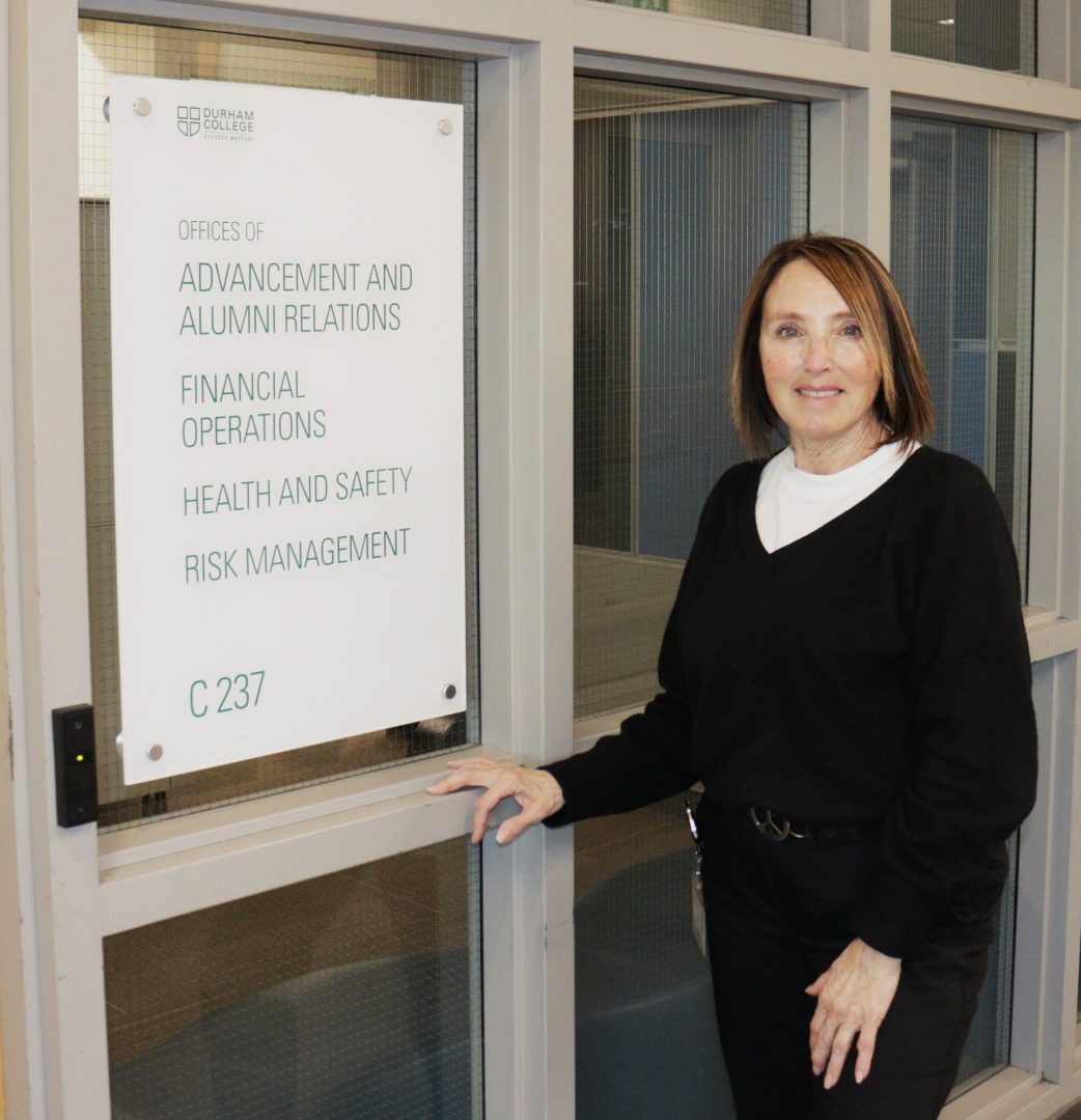 A woman with red hair and a white shirt under a black sweater poses for a picture in front of a window.