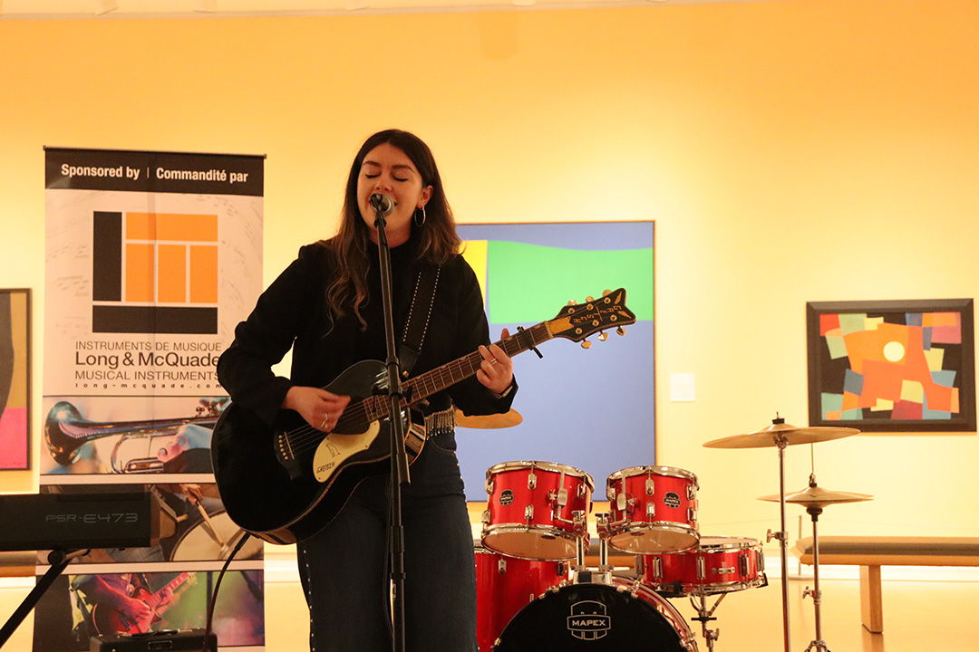 Woman singing with her eyes closed while playing gutair in an art gallery.