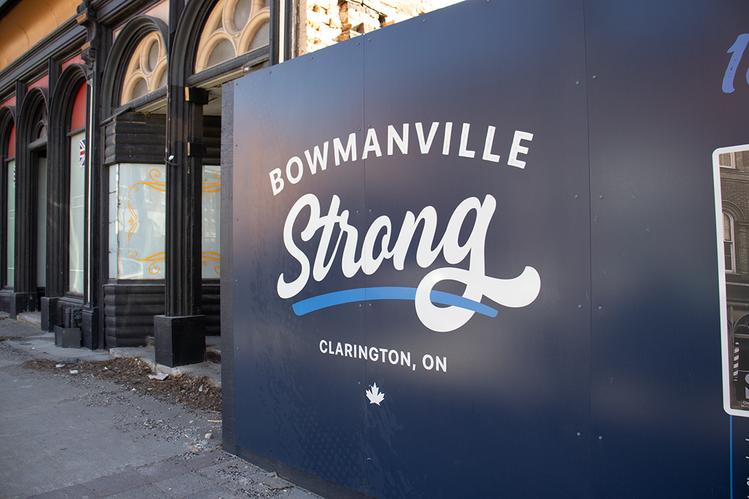 A blue and white wooden sign that says "Bowmanville Strong" covers an opening left by a fire between two buildings.