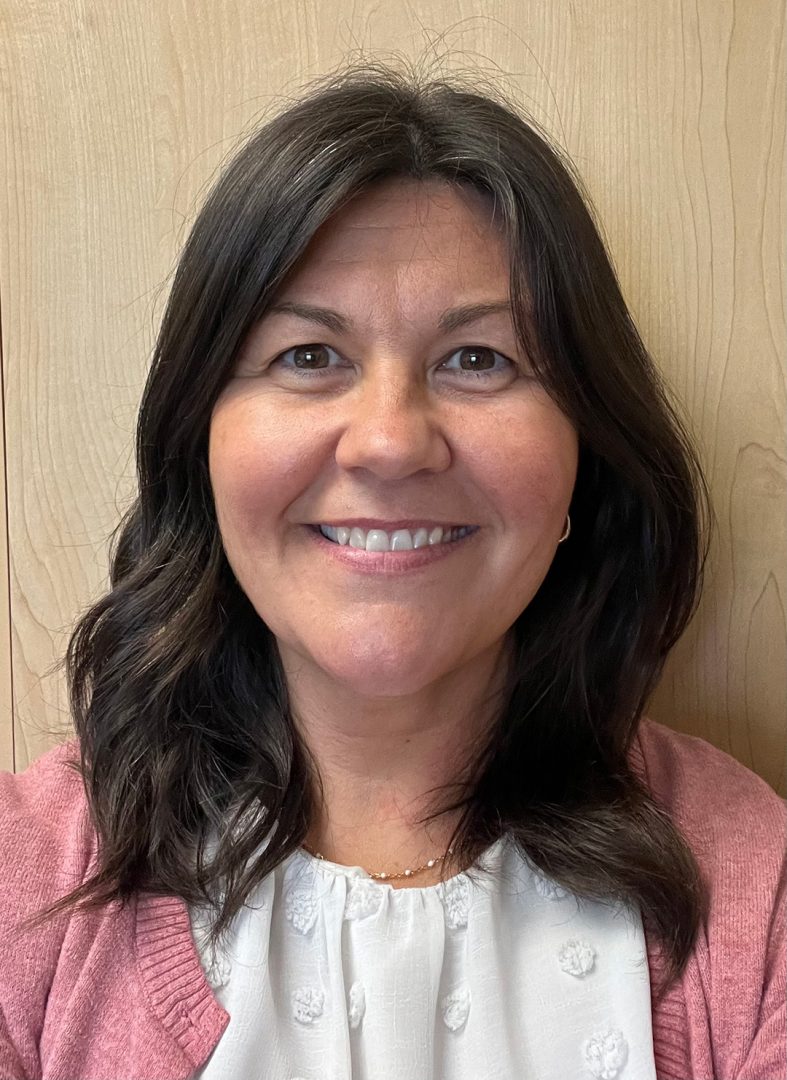 A woman wearing a white shirt and pink cardigan is smiling.