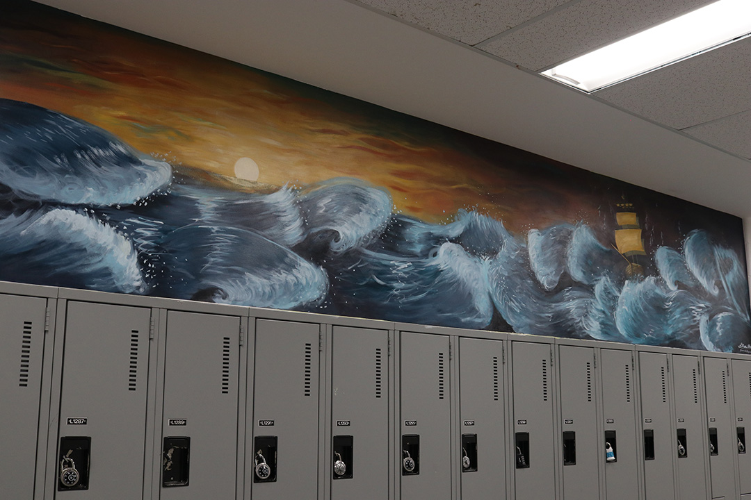 Blue waves crash as they rock a boat in the rough sea, during sunset in a painting created above a row of sliver lockers.