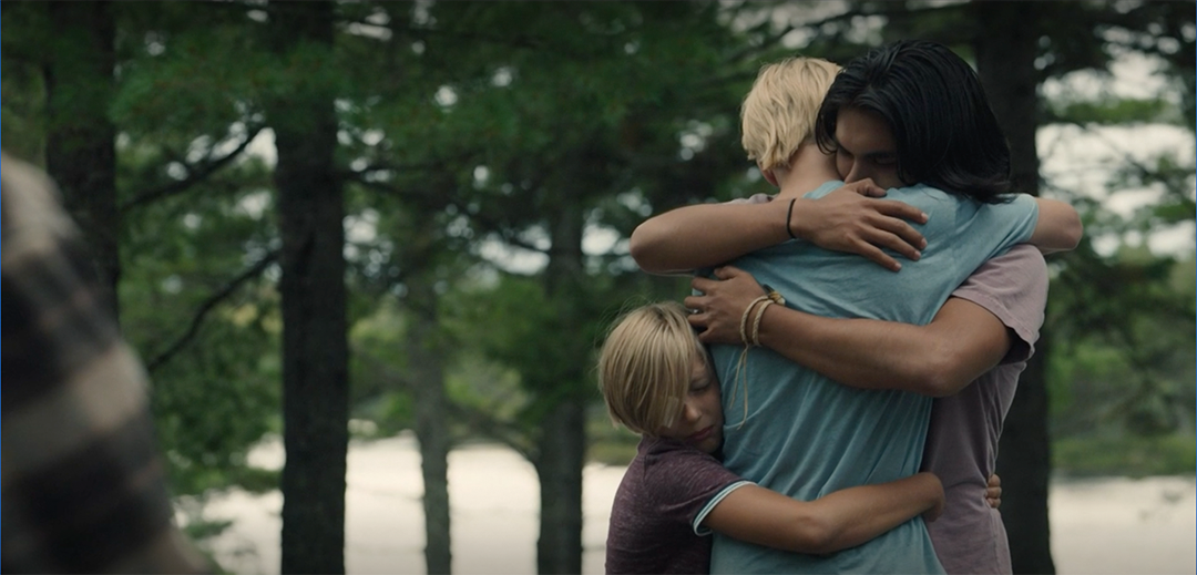three young guys hugging eachoter, trees and lake behind them