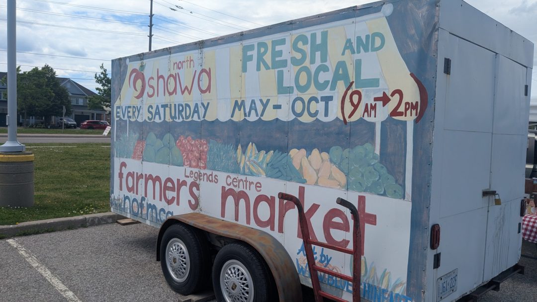 A trailer with a painted sign advertising the North Oshawa Farmers’ Market.