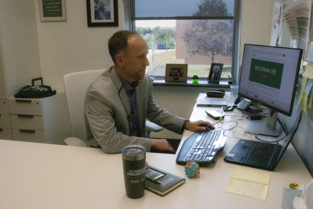 A man wearing a grey suit jacket looks at a computer screen.