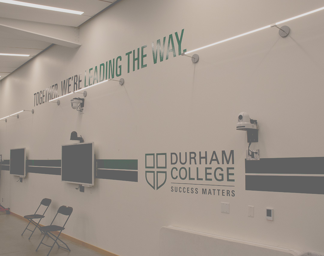 A white wall with green letters. There's a sign that says Durham College Success Matters. There is also lettering that says Together We're Leading the Way.